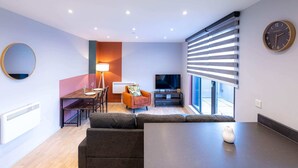 A modern living room with a sofa, a dining table, and a TV. - Victoria Park Vista One-bedroom by Sojo Stay (London)