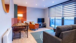 A modern living room with a dining area, a flat-screen TV, and large windows with blinds. - Victoria Park Vista One-bedroom by Sojo Stay (London)