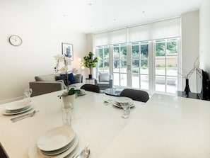 Enjoy meals in a serene garden-view setting with a large dining table and a clock on the wall.
