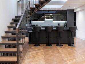 Une cuisine moderne dotée d’un îlot central, de tabourets de bar et d’un escalier avec des rampes en métal.