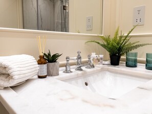 Un bagno con un lavandino in marmo bianco, uno specchio, una pila di asciugamani, una pianta in vaso e articoli da toilette.