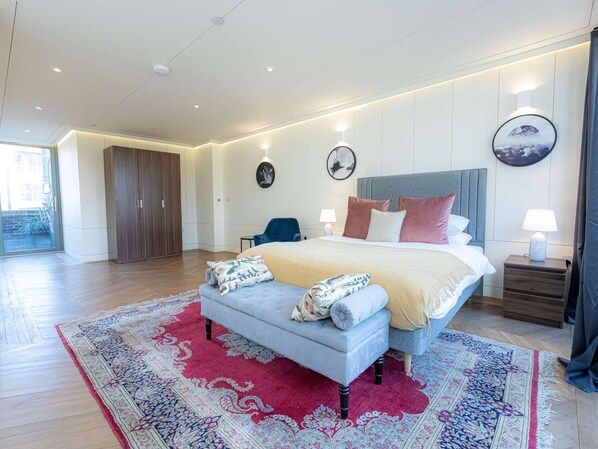 Una camera da letto moderna con un letto grande, un divano grigio, un tappeto con motivo rosso e blu e un'armadio in legno.