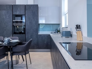 A modern kitchen with dark cabinetry, a built-in oven, a sink, and a dining area with a table and chairs. - Family Fun in Camden (London)