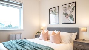 Una cama bien tendida con un edredón verde, un cabecero gris y dos lámparas de noche.