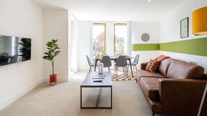 A modern living room with a brown leather sofa, a coffee table, and a dining area with chairs and a table. - Horniman Museum Harmony Two-bedroom by Sojo Stay (Mitcham)