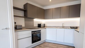 A modern kitchen with white cabinets, a built-in oven, a microwave, and a toaster. - Horniman Museum Harmony Two-bedroom by Sojo Stay (Mitcham)