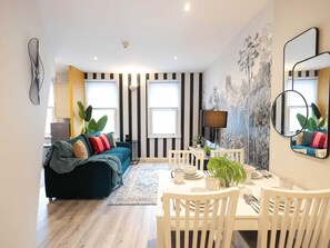 A modern living room with a sofa, dining table, chairs, and a large window.