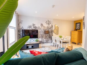 A modern living room with a flat-screen TV, a dining area with a white table and chairs, and a kitchen area with a wooden cabinet. - Explore Granary Square Two Bedroom by Belvilla (London)
