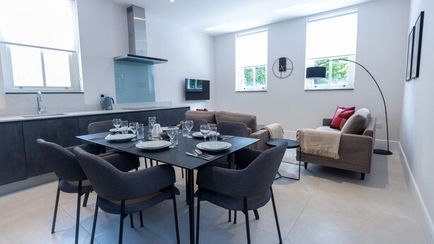 A modern kitchen with a dining area, large windows, and a living space with a sofa and a floor lamp. - Culinary Delights 3-bedroom (London)