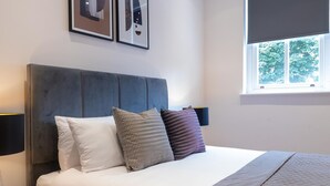 A bedroom with a bed, a headboard, a window, and framed artwork on the wall. - Culinary Delights 3-bedroom (London)