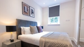 A modern bedroom with a bed, bedside table, lamp, and artwork on the wall. - Culinary Delights 3-bedroom (London)