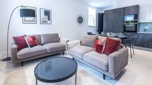 A modern living room with two sofas, a glass coffee table, and a dining area with a kitchen in the background. - Culinary Delights 3-bedroom (London)