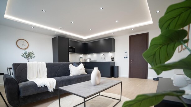 Een moderne woonkamer met een donkergrijze bank, een salontafel en een keuken op de achtergrond.