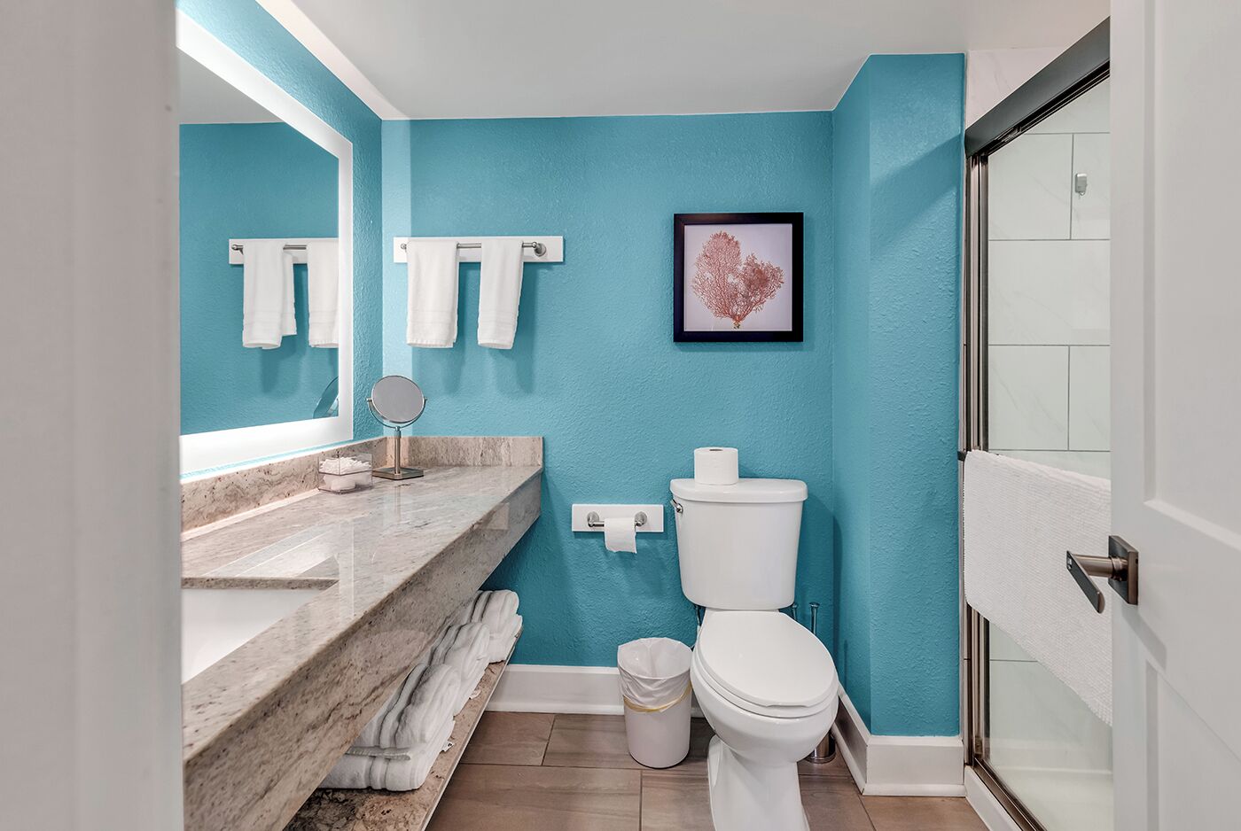 Une salle de bain avec un mur bleu, un lavabo en marbre, des toilettes et un tableau encadré.