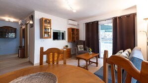 A living room with a wooden dining table, chairs, a sofa, and a TV.