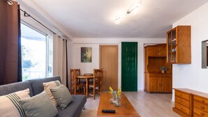 A living room with a sofa, a dining table, and a kitchen area with wooden cabinets.