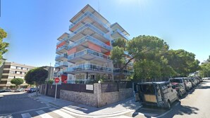 A multi-story residential building with balconies, a gated entrance, and parked cars along the street.