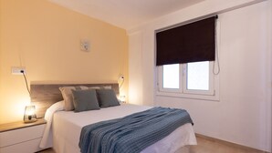 A bedroom with a bed, bedside tables, a window with a blind, and a wall-mounted light switch.