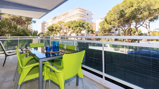 A balcony with a table and chairs, overlooking a street with buildings and trees.