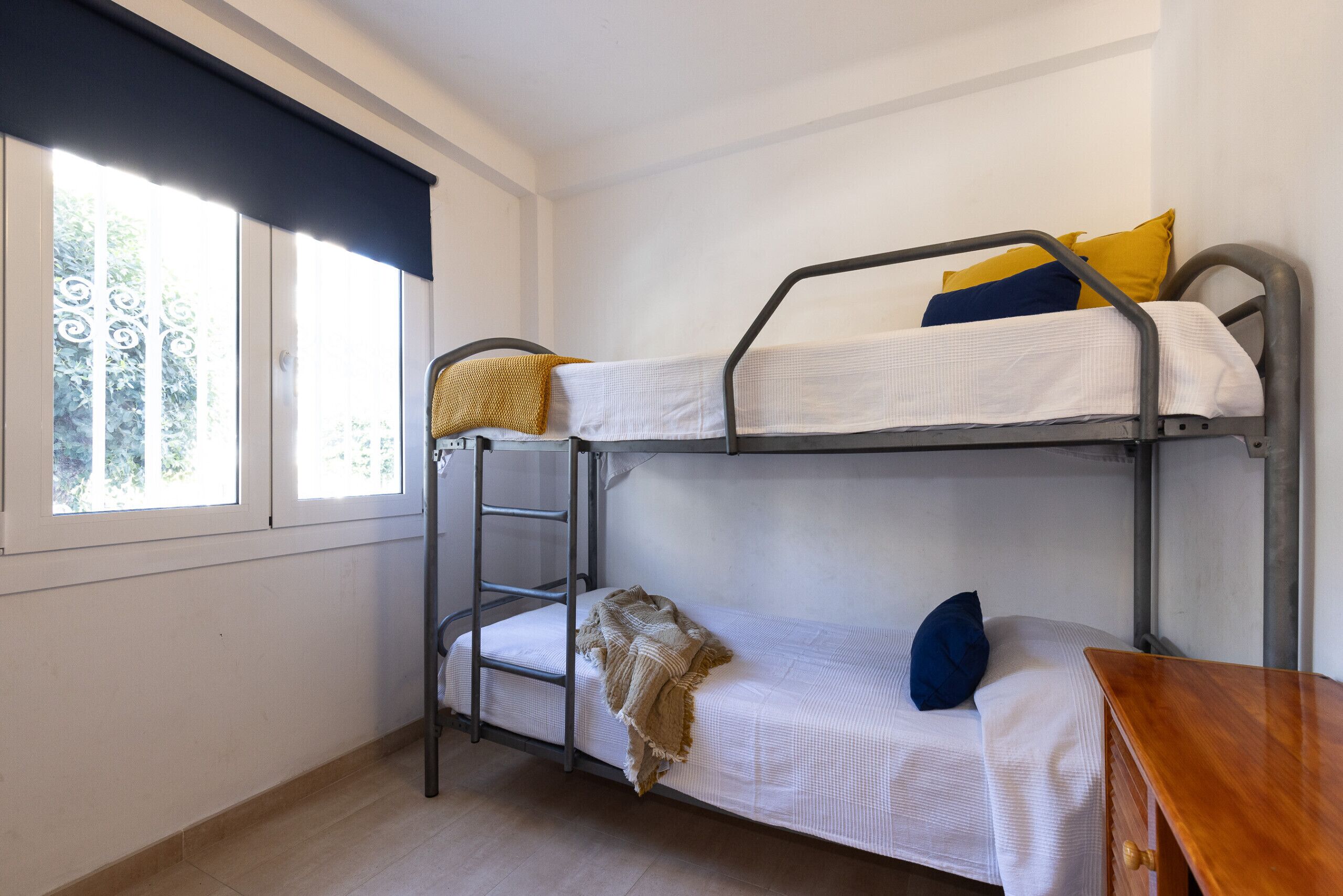 A bunk bed room with a window, a wooden table, and a metal ladder.