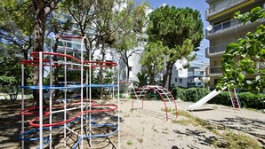 A playground with climbing structures and a slide, surrounded by trees and a building. - Cosy Apartment near Beach · AirCon · Pool · UHC PINO ALTO 187 (Salou)