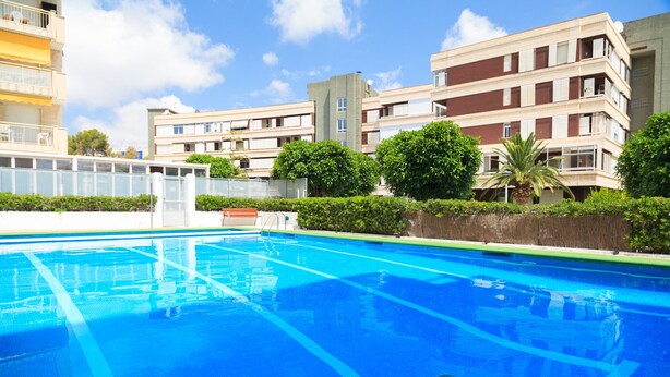 A swimming pool with clear blue water, surrounded by greenery and modern buildings. - Cosy Apartment near Beach · AirCon · Pool · UHC PINO ALTO 187 (Salou)