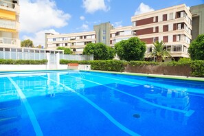 A swimming pool with clear blue water, surrounded by greenery and modern buildings.