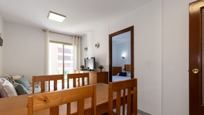 A compact room with a wooden dining table, chairs, a bed with a blue pillow, a desk with a computer and plants, and a large mirror on the wall. - Cosy Apartment near Beach · AirCon · Pool · UHC PINO ALTO 187 (Salou)