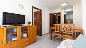 A living room with a TV on a wooden cabinet, a dining table with chairs, and a sofa. - Cosy Apartment near Beach · AirCon · Pool · UHC PINO ALTO 187 (Salou)