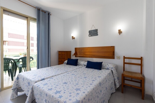 A bedroom with two beds, a wooden headboard, a chair, and a balcony with chairs.