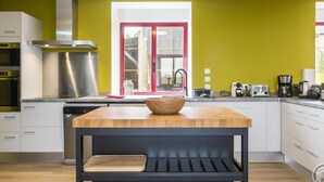 A modern kitchen with white cabinets, a stainless steel range hood, a wooden table with a cutting board, and a window with a red frame. - Spacious 5-bedroom countryside house, pet-friendly, parking, internet included, near Mont St-Michel (Saint-Laurent-de-Terregatte)