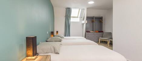 A bedroom with two beds, a bedside table with a lamp, a wardrobe, and a window with curtains.