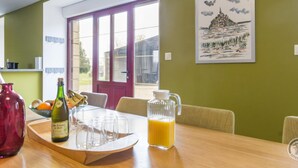 A dining area with a table set for two, a bottle of orange juice, and a pitcher. A window with a view of the outside is visible. - Spacious 5-bedroom countryside house, pet-friendly, parking, internet included, near Mont St-Michel (Saint-Laurent-de-Terregatte)