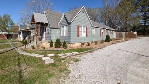 A two-story house with a front porch, a small front yard, and a gravel driveway.