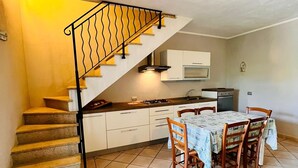 A kitchen with a dining table and chairs, a staircase with a railing, and a microwave above the counter. - Le Querce 5 DX (San Teodoro)