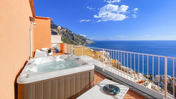 A balcony with a hot tub, outdoor seating, and a view of the sea. - BlueVista Home -Terrace Jacuzzi/Hot Tub (Positano)