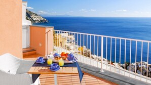 A balcony with a table set for breakfast, overlooking a coastal view. - BlueVista Home -Terrace Jacuzzi/Hot Tub (Positano)