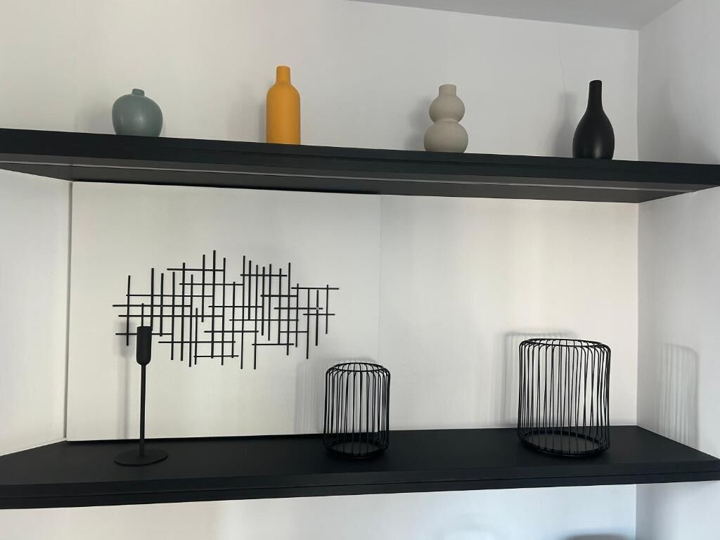 Un interior moderno con dos estantes negros, uno con un jarrón negro y el otro con un candelabro negro.