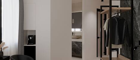 A modern hotel room with a bed, a desk with a computer, a chair, a wardrobe, and a bathroom visible through an open door.