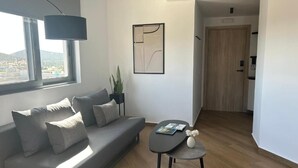 Una sala de estar moderna con un sofá gris, una mesita de centro pequeña, una planta en maceta y una obra de arte abstracta enmarcada en la pared.