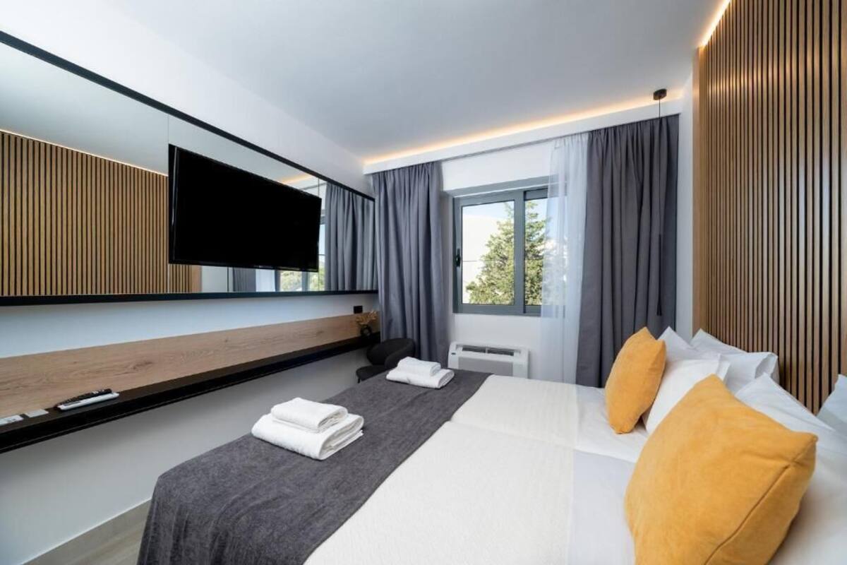 A modern hotel room with a large bed, a flat-screen TV mounted on the wall, and a window with curtains.