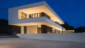 Una casa moderna de dos pisos con techo plano, ventanas amplias y un balcón.