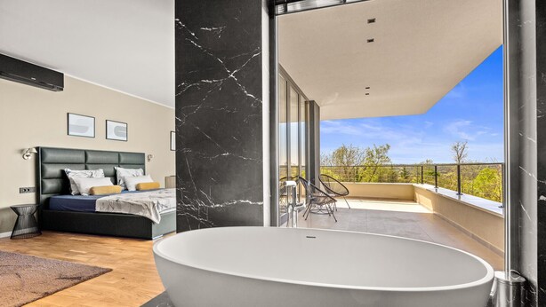 Un dormitorio moderno con una cama grande, un baño con bañera independiente y un balcón con mobiliario de exterior.