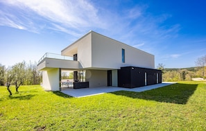 Uma casa moderna de dois andares com telhado plano, janelas amplas e uma varanda.
