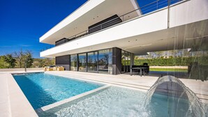 Una casa moderna con piscina, mobiliario exterior y un amplio frente de cristal.
