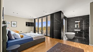 Un dormitorio moderno con cama, televisor, balcón y baño con bañera.