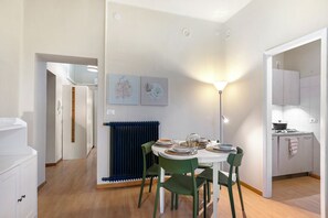 A modern kitchen with a dining area, featuring a round table with chairs, a blue radiator, and two wall-mounted artworks.