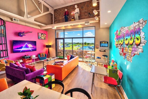 Un lobby de hotel vibrante con un amplio ventanal que ofrece vistas a un campo de golf, un mural de pared colorido y una zona de estar con una combinación de sofás y mesas.