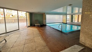 Et moderne poolområde indendørs med uhindret udsigt til det fri, en liggestol og en pool med metalstige.