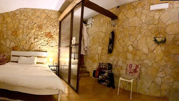 Une chambre avec un mur en pierre, un lit, une chaise et une armoire.